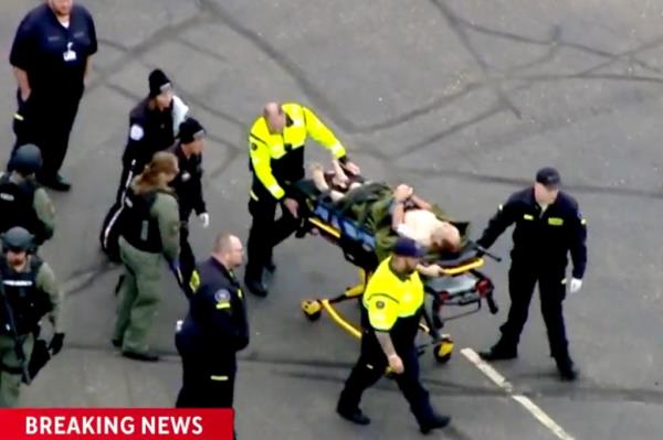 A person in police custody getting taken away on a stretcher.