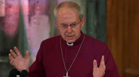 Reuters The Archbishop of Canterbury, dressed in a maroon cassock and a wearing a large silver cross on a chain, gestures with his hands as he speaks during the annual Lord Mayor's Banquet at Guildhall in London