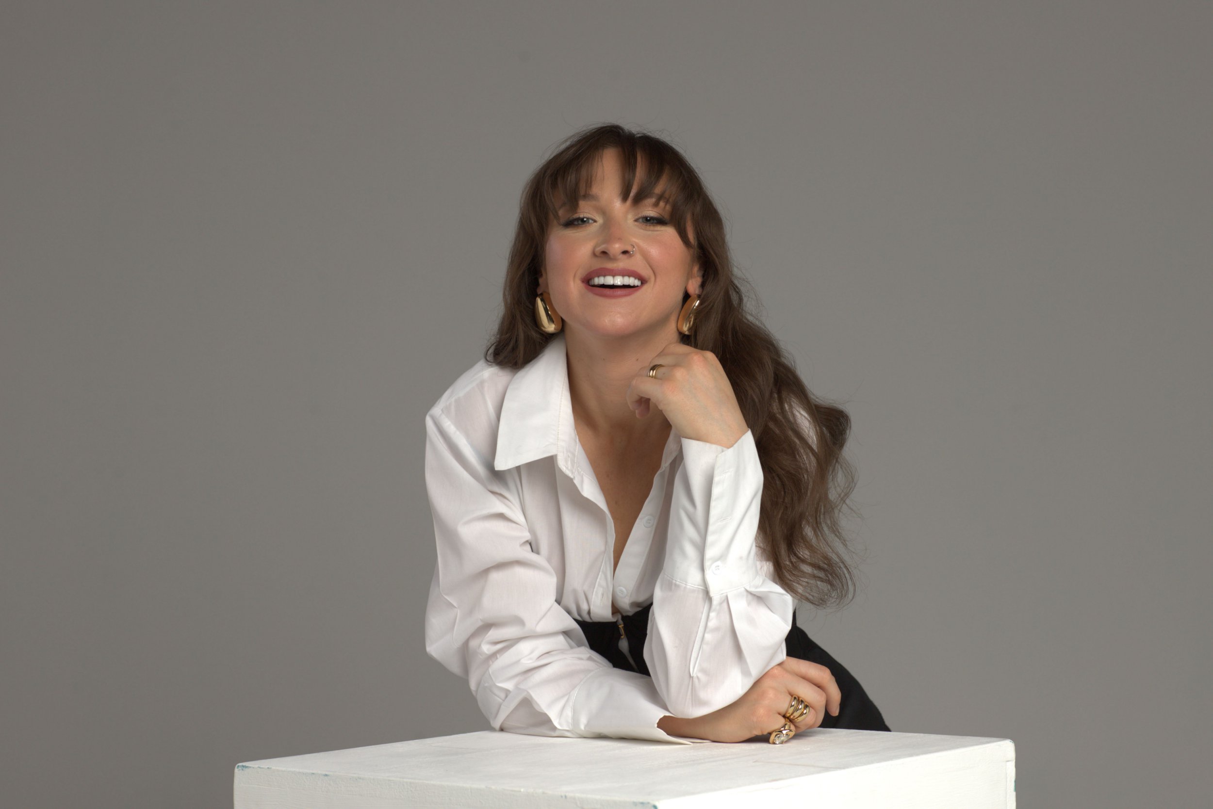 Sydnie Christmas leaning on a table while wearing a white shirt. She is smiling.