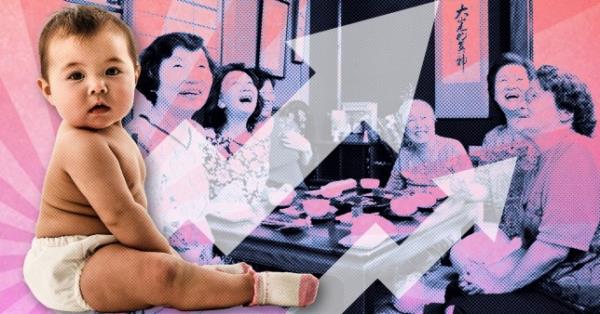 A baby wearing a nappy with a group of older Japanese people laughing and smiling in the background