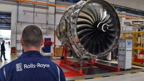 Getty Images A Rolls-Royce worker looks on at a huge jet engine inside a factory