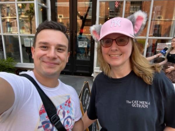 A man and a woman, who is wearing a pink hat with ears, smile for a selfie outdoors.