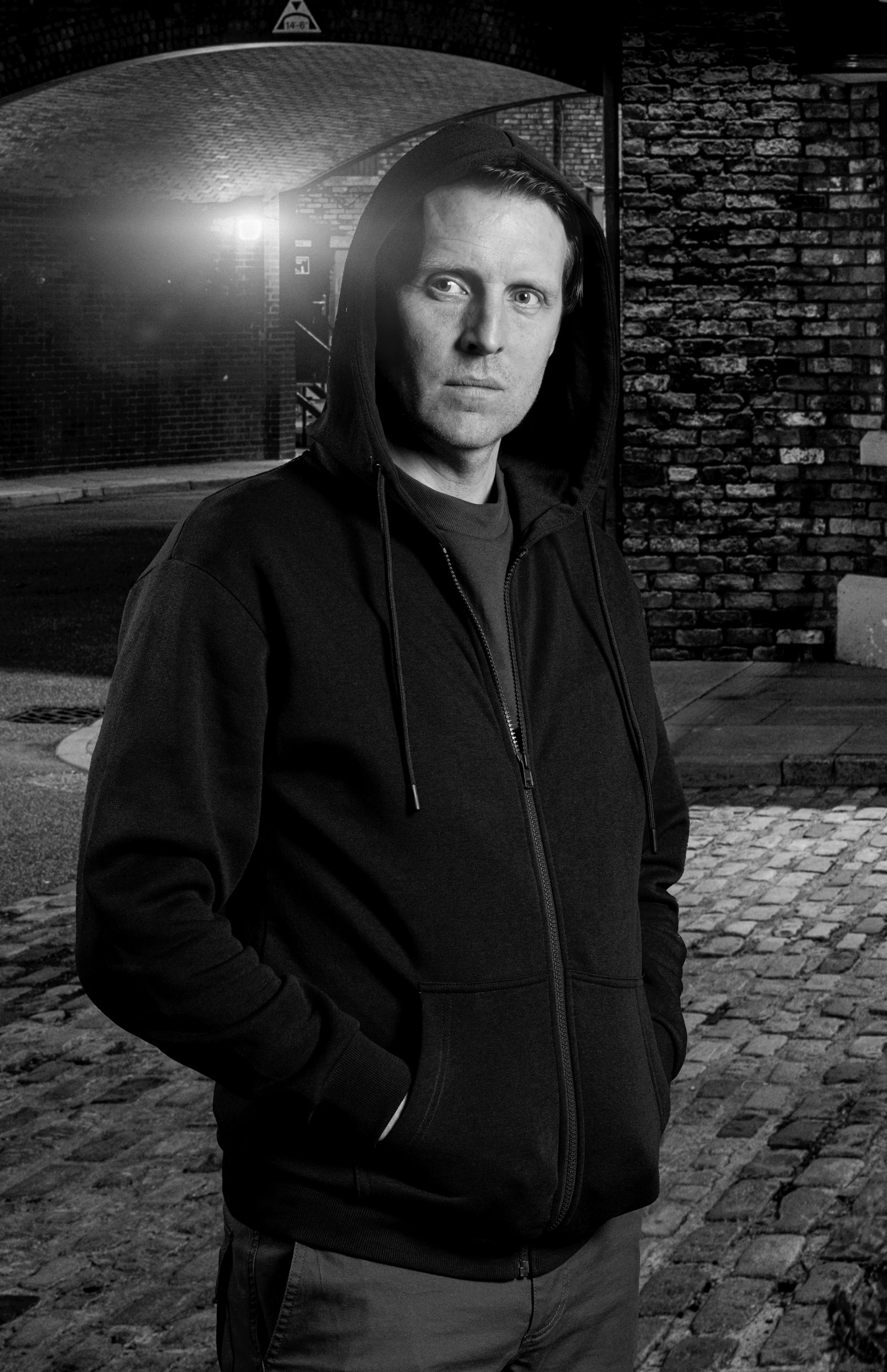 Nathan Curtis looks away from the camera in a dark hoodie in Coronation Street