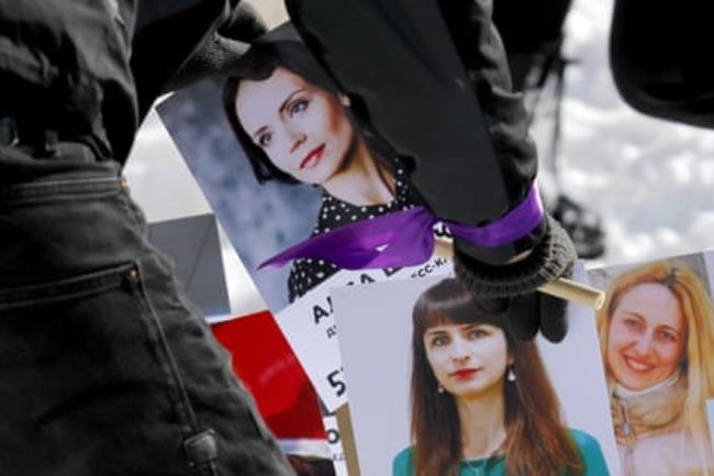 A person wearing a purple ribbon on their wrist places photographs of women in a display