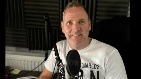 Dean Booty Podcaster Dean Booty sitting in a studio in front of a microphone
