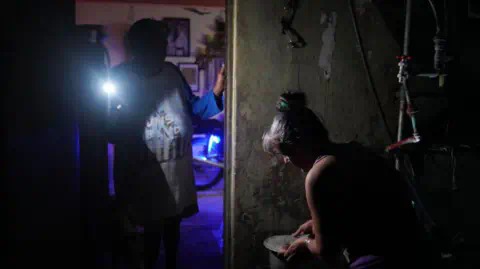 AFP A woman boils water while another lights her with a mobile phone during a nationwide blackout caused by a grid failure in Matanzas, Cuba, on October 18, 2024.