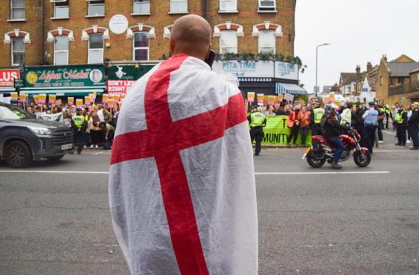 A lone right-wing protester draped in an England flag watches as crowds gather for a rally against the far-right