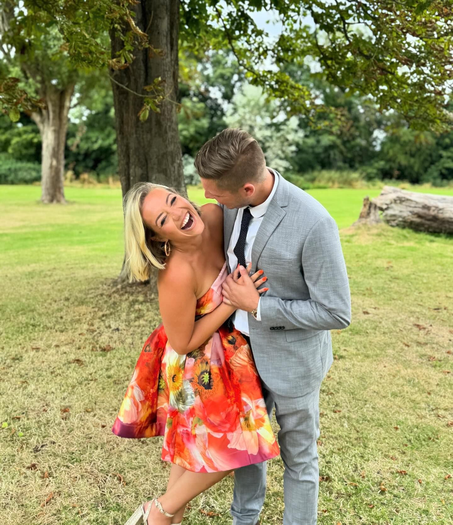 Kelsey Parker smiling and laughing with her arm wrapped around a man. She is waring a floral dress while he is wearing a grey suit