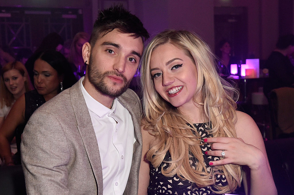 Tom Parker and Kelsey Parker posing at an event. Tim is wearing a grey suit jacket and a white shirt while Kelsey is wearing a blue lace dress
