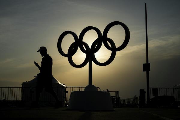 The sun sets behind a statue of the Olympic rings, silhouetting them and a man walking past 