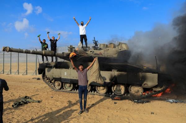 Palestinians celebrate as an Israeli military vehicle burns after it was hit by Palestinian gunmen who infiltrated areas of southern Israel, at the Israeli side of Israel-Gaza border, October 7, 2023