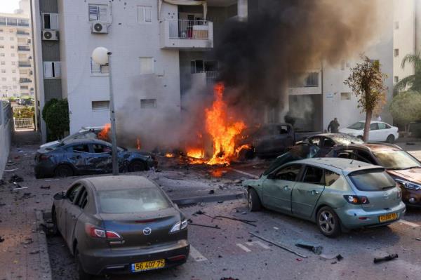 A member of the Israeli security forces stands near burning cars following a rocket attack from the Gaza Strip in Ashkelon, southern Israel, on October 7, 2023