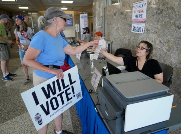 Karan Navak (left), of Milwaukee, is handed a ballot by poll worker, Wendy Centeno, before voting as part of early voting at the Frank P. Zeidler Municipal Building on North Broadway in Milwaukee on Tuesday, July 30, 2024.