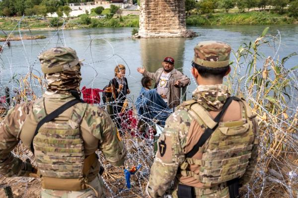 Texas National Guard troops speak with a Venezuelan migrant after he crossed the Rio Grande from Mexico into the US.