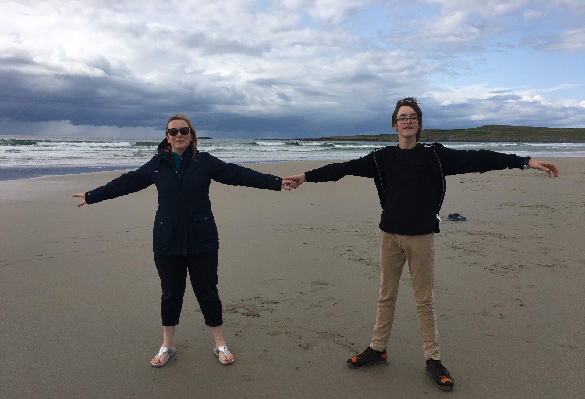 Julie and James at a beach, holding hands, with their other arms extended out to the side