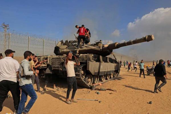 A group of male Palestinian militants take selfies in front of and climb over a captured Israeli tank.