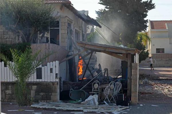 A house in the southern Israeli city of Ashkelon burns following a rocket attack, and a man in the background is seen running for cover.