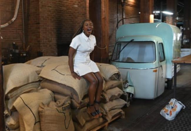 A woman sits on a pile of large coffee bags