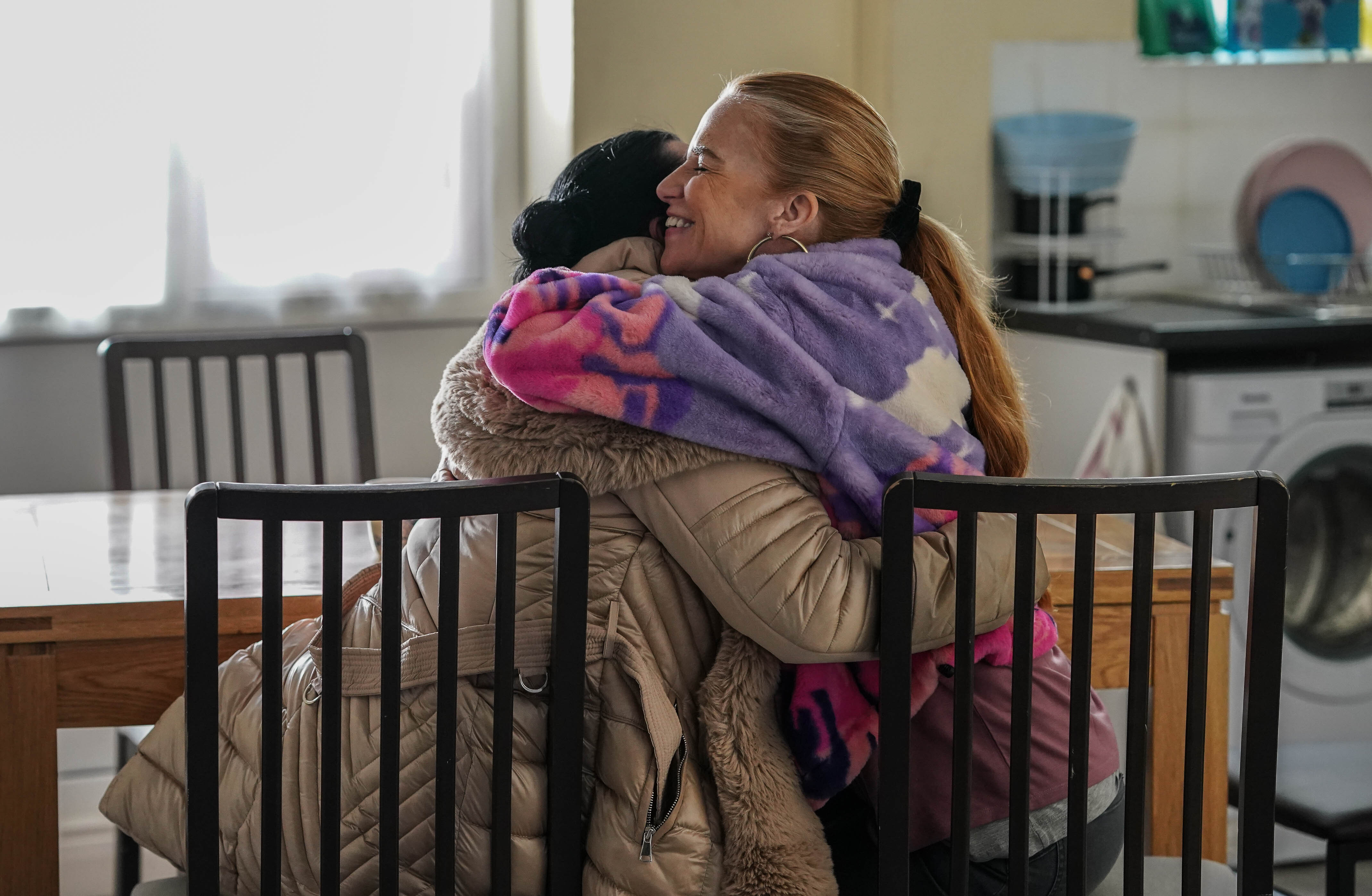 Bianca and Whitney hugging while sitting at a kitchen table in EastEnders
