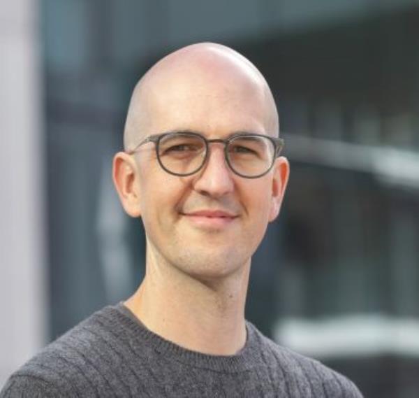 Portrait photo of a bald white man wearing glasses and a grey jumper.