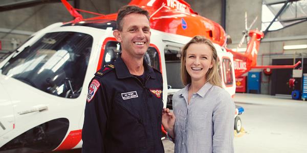 Two person are standing beside a helicopter inside a hangar.