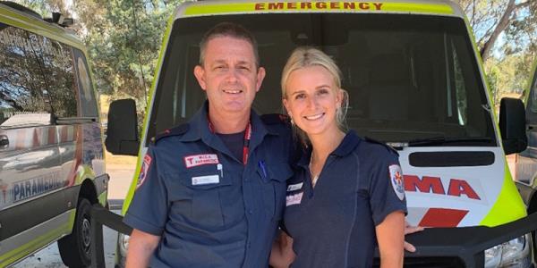 Two people standing in front of an ambulance parked in an open carport.