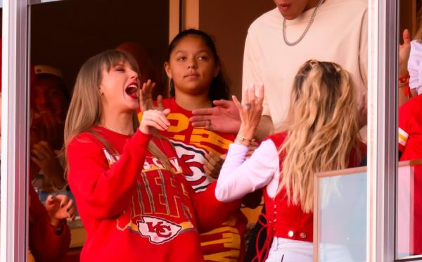 Taylor swift and Brittany Mahomes celebrate a Travis Kelce touchdown with people in the background.
