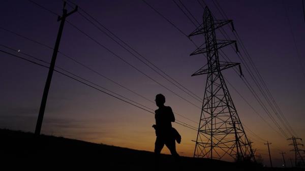 FILE - A jogger passes power lines during a sunset run, Aug. 20, 2023, in San Antonio, as high temperatures continue to stress the power grid. On Thursday, Sept. 7, Texas' power grid manager again asked residents to cut back on electricity as a prolonged and punishing summer heat wave continued, a day after the system was pushed to brink of outages for the first time since a deadly winter blackout in 2021. (AP Photo/Eric Gay, File)