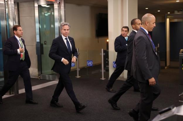 A man in a suit with grey hair walks in a corridor surrounded by other men.