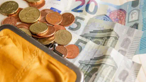 Getty Images A yellow purse with Euro notes and coins spilling out.