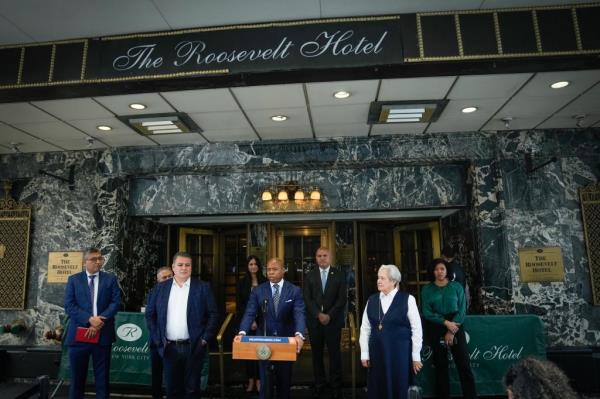 New York City Mayor Eric Adams speaking at a press conference outside the Roosevelt Hotel in Manhattan, with national Latino leaders and other individuals nearby