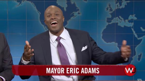 New York City Mayor Eric Adams in a suit and tie on SNL's Weekend Update, questioning Michael Che about his perceived guilt