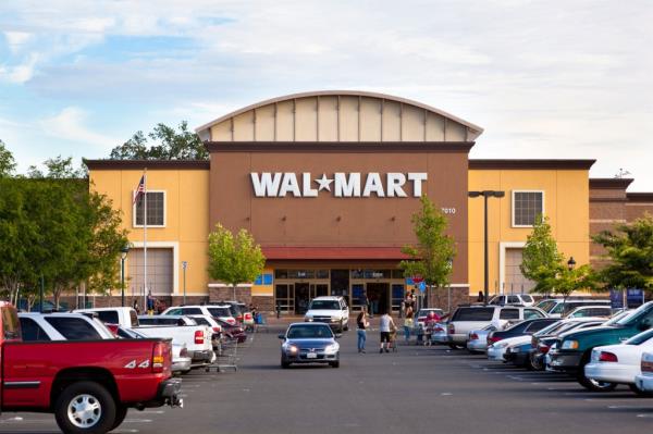 The outside of a Walmart store with parking lot and shoppers about.