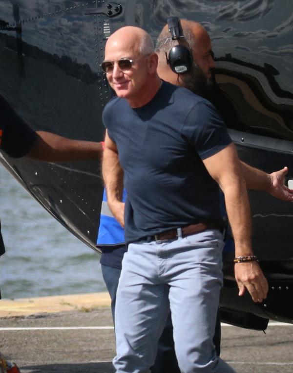 Jeff Bezos and Lauren Sanchez arriving at a Heliport in New York City, with Lauren Sanchez having flown the helicopter herself, and now walking alongside a bullet-proof vehicle with Bezos' security detail around them.