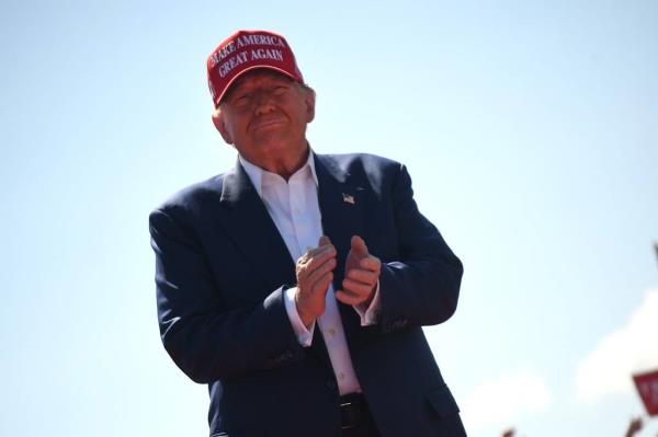 Donald Trump in a suit and hat, speaking to a large crowd at Wilmington International Airport during his 2024 campaign event.