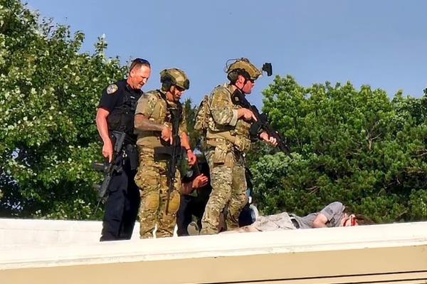 身穿迷彩服和警服的警察在托马斯·马修·克鲁克斯的尸体旁。