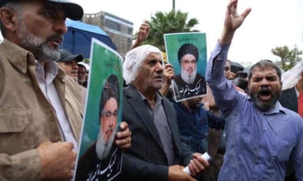 Men, wet from rain, holding pictures of Nasrallah