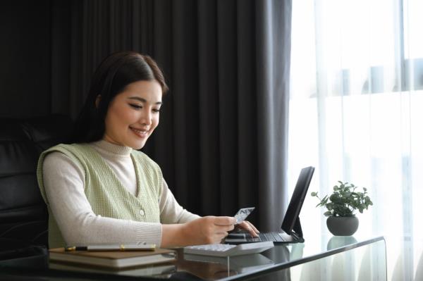 Young woman holding a credit card and calculating expenses on a laptop at home
