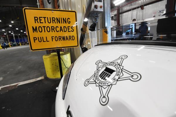 Inside the Secret Service's secured logistics hub storing fleet for mobile security, featuring a yellow sign next to a white car