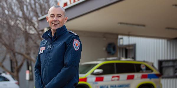 A man wearing a blue jacket standing in front of an ambulance building.