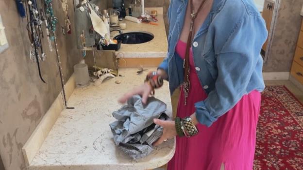 A woman holding a pile of gray men's clothes.