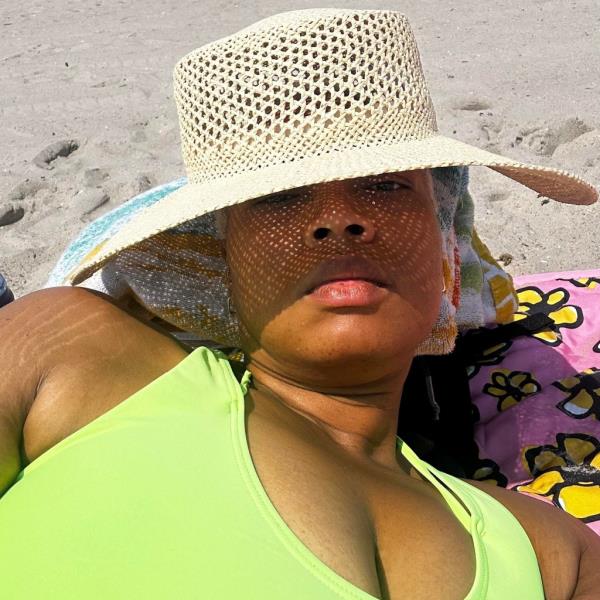 Mishawn Jack laying on beach in a green bathing suit and straw hat pulled down over her eyes