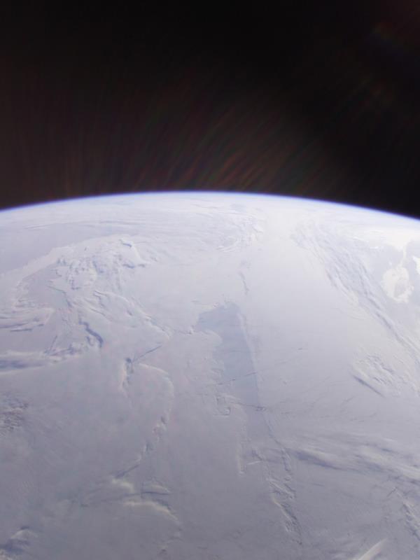从太空看极地覆盖的雪景，地球的曲率在黑暗背景下沿着地平线可见。