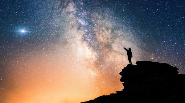 Person on cliff reaching toward sky