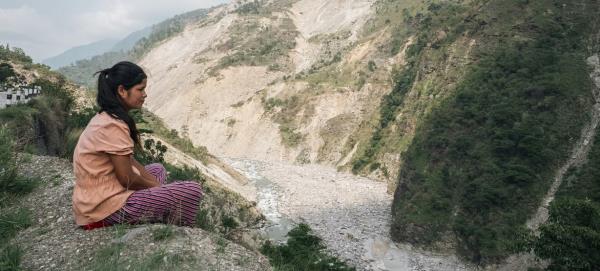 In western Nepal, a girl sits on the edge of a cliff, overlooking a massive landslide brought on by the monsoon rains in 2023.