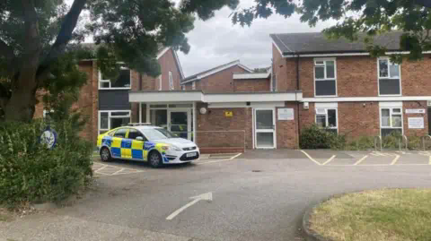 本·帕克/英国广播公司 警车停在一栋红砖的双层住宅区外。建筑前有一个停车场和一片绿色草地。
